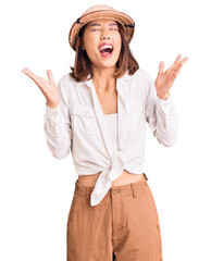 Young beautiful chinese girl wearing explorer hat celebrating mad and crazy for success with arms...