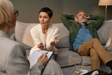 Portrait of mature adult woman talking to female psychologist in couples therapy session with...