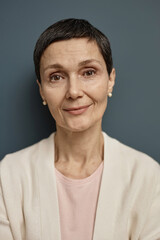 Fototapeta premium Vertical closeup portrait of mature woman looking at camera against grey background with smile