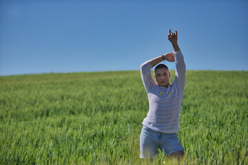 Young, South American, non-binary person, heavily makeup, posing in a white sweater with natural daisies, in the middle of a green wheat field, with one arm raised. Concept queen, lgbtq+, pride, queer