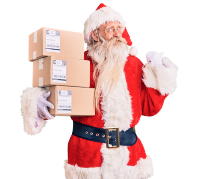 Old senior man with grey hair and long beard wearing santa claus costume holding boxes pointing thumb up to the side smiling happy with open mouth