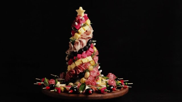 Appetizers board with different antipasti, charcuterie, snacks and cheese. Christmas tree of meat, sausage delicacies and cheese on a kraft wooden board. Christmas decor on black background.