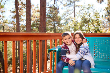 Fototapeta premium Two Siblings sit on a chair on a porch in the woods.