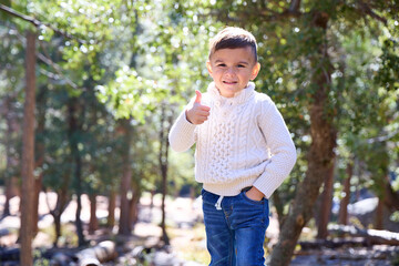 A young boy hangs out in the forest wearing a sweater