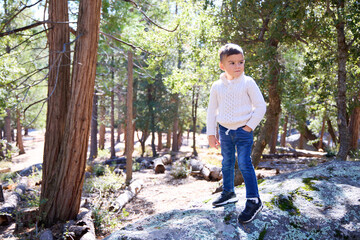A young boy hangs out in the forest wearing a sweater