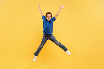Fototapeta na wymiar Ecstatic boy jumping high with arms up on yellow background