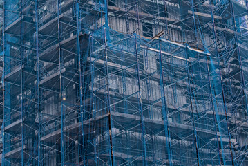 building under construction covered in blue mesh tarp protective wrap (safety debris netting during...
