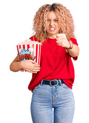 Young blonde woman with curly hair eating popcorn annoyed and frustrated shouting with anger, yelling crazy with anger and hand raised