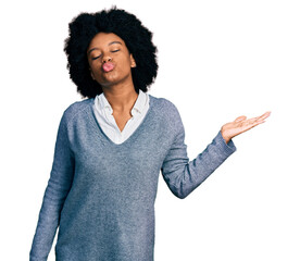 Young african american woman presenting with open palm looking at the camera blowing a kiss being...