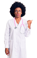 Young african american woman wearing doctor coat and stethoscope surprised pointing with hand finger to the side, open mouth amazed expression.