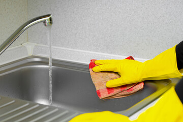 Hand of woman cleaning the kitchen counter and sink at home.