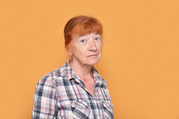Senior woman with red hair and freckles on face with thoughtful look on yellow background, woman...