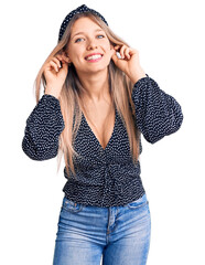 Young beautiful blonde woman wearing casual clothes smiling pulling ears with fingers, funny...