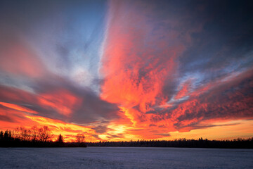 Fototapeta premium Colourful sunrise with glowing red clouds on a winter's day over the meadows and forests of Siebenbrunn, the smallest district of the Fugger city of Augsburg