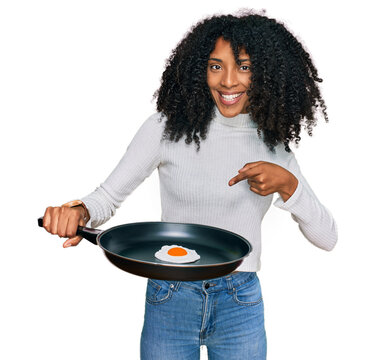 Young african american girl holding skillet with fried egg smiling happy pointing with hand and finger
