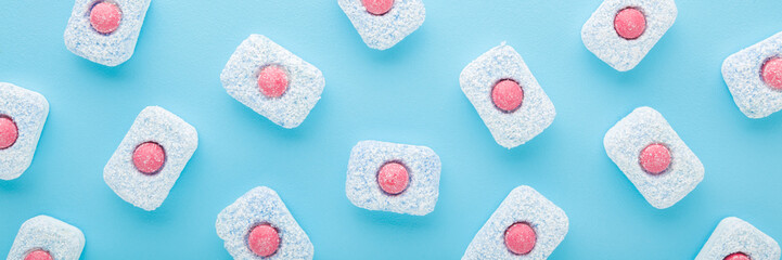 Red white blue dishwasher tablets on light blue table. Wide banner. Pastel color. Closeup. Top down...