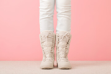 Girl long legs in white jeans and beige warm winter boots standing and posing on light carpet at pink wall background. Pastel color. Closeup. Front view.