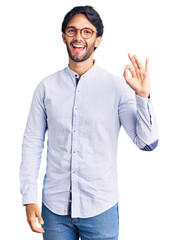 Handsome hispanic man wearing business shirt and glasses smiling positive doing ok sign with hand and fingers. successful expression.