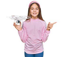 Beautiful brunette little girl using drone smiling happy pointing with hand and finger to the side