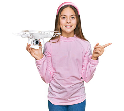 Beautiful brunette little girl using drone smiling happy pointing with hand and finger to the side