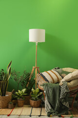 Armchair with lamp and houseplants near green wall in room