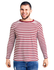 Young handsome man wearing striped sweater winking looking at the camera with sexy expression, cheerful and happy face.