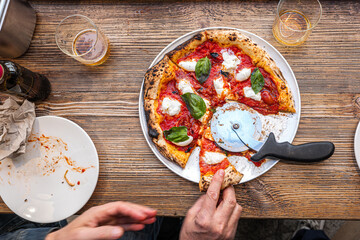 Male hand taking a slice of freshly baked Neapolitan Margherita Pizza on a rustic wooden table in a...