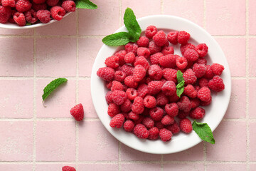 Plate with fresh raspberries and mint on pink tile background