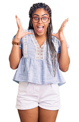 Young african american woman with braids wearing casual summer clothes and glasses celebrating crazy and amazed for success with arms raised and open eyes screaming excited. winner concept