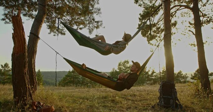 Aesthetic rest. A beautiful young girl and her boyfriend are relaxing in hammocks at sunset.