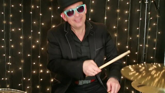Drummer in glasses and hat plays drum set at studio with garlands