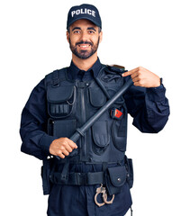 Young hispanic man wearing police uniform holding baton pointing finger to one self smiling happy...