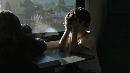 Tired Litle boy rubbing eyes and face while on a moving train hiding from sun rays. Passenger Child...
