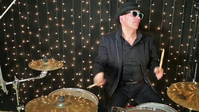 Drummer with glasses and in hat plays drum set at studio.