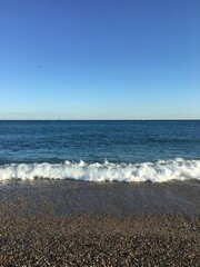 Toma vertical de una playa de guijarros con el cielo azul de verano y olas rompiendo en la orilla en Barcelona, España.