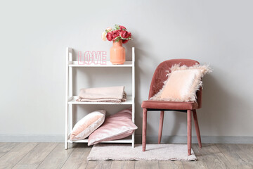 Cozy chair and vase with bouquet of beautiful artificial flowers on shelving unit near white wall
