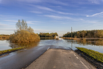 A truck is driving along a flooded road. Natural disaster, spring flood. A road in a rural area is...
