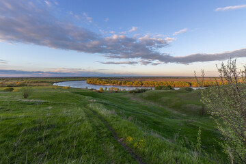 Colorful rural landscape with a path leading to a wide river, Lots of green grass in the foreground.