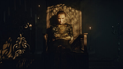 A young woman in a black long dress sits in a wooden carved throne in a dark Gothic church