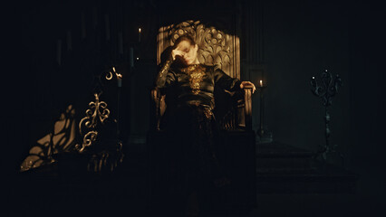 A young woman in a black long dress sits in a wooden carved throne in a dark Gothic church