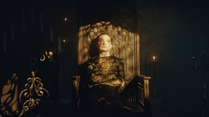 A young woman in a black long dress sits in a wooden carved throne in a dark Gothic church