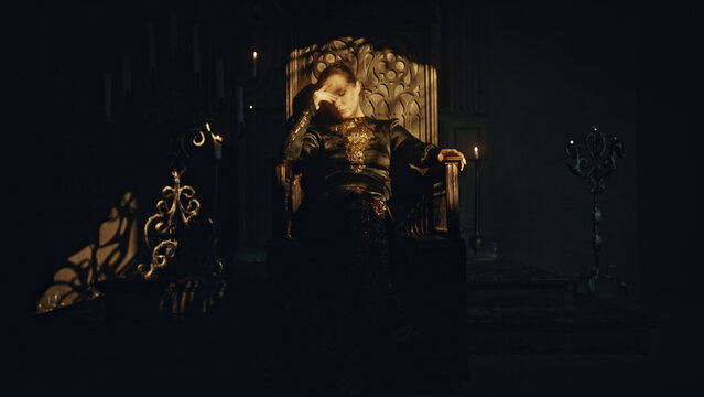 A young woman in a black long dress sits in a wooden carved throne in a dark Gothic church