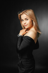 Fototapeta premium Portrait of a young blonde woman standing on a black background in a stylish elegant dress, looking at the camera with a smile on her face, smiling confidently cutely.