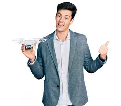 Young hispanic business man holding drone pointing thumb up to the side smiling happy with open mouth