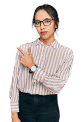 Young hispanic girl wearing casual clothes and glasses pointing with hand finger to the side showing advertisement, serious and calm face