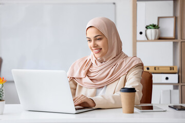 Pretty Muslim female programmer using laptop in office