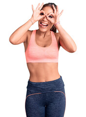 Young beautiful hispanic woman wearing sportswear doing ok gesture like binoculars sticking tongue out, eyes looking through fingers. crazy expression.