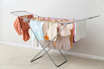 Clean baby clothes hanging on dryer near white wall