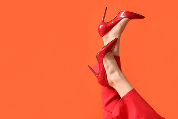 Legs of young woman in stylish red high heels on orange background