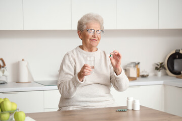 Senior woman with pill and glass of water in kitchen